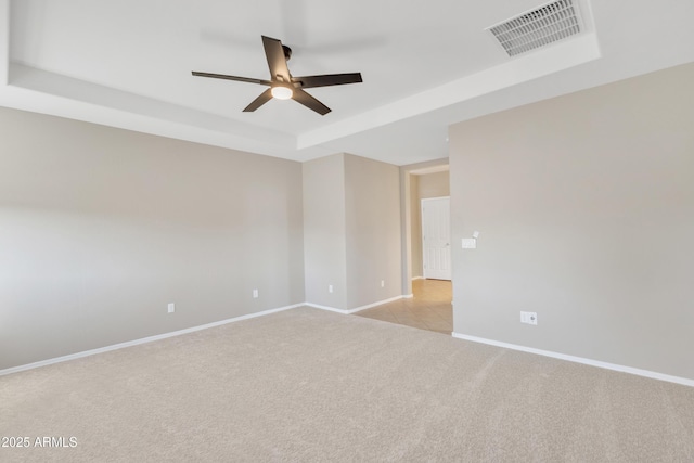 unfurnished room featuring light carpet, a tray ceiling, and ceiling fan