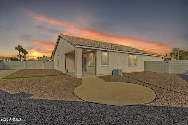 back house at dusk with central AC and a patio area