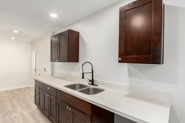 kitchen featuring dark brown cabinetry, light wood-style floors, light countertops, and a sink