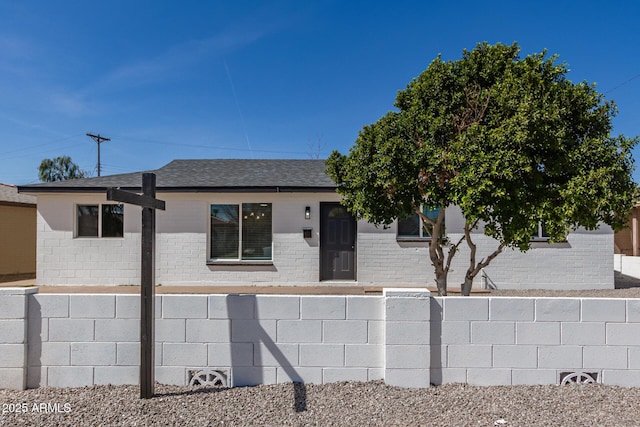 view of front of house featuring a shingled roof, brick siding, and fence