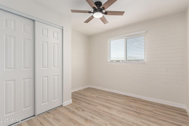 unfurnished bedroom featuring a closet, ceiling fan, brick wall, light wood-type flooring, and baseboards