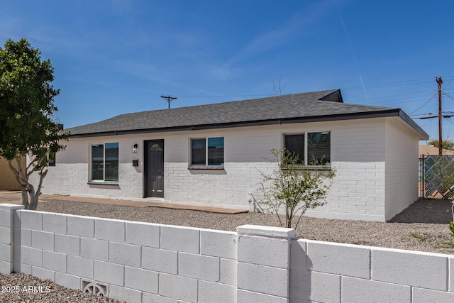 ranch-style house featuring a shingled roof, fence, and brick siding