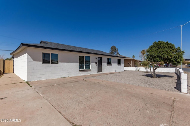 ranch-style home with concrete block siding, fence, and roof with shingles