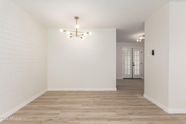 spare room with a chandelier, brick wall, light wood finished floors, and baseboards