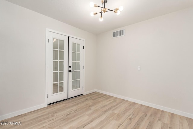 spare room with a notable chandelier, wood finished floors, visible vents, baseboards, and french doors