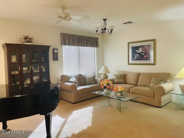 carpeted living room with visible vents and ceiling fan with notable chandelier