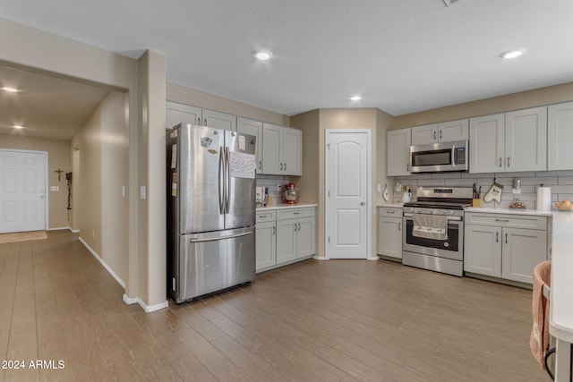 kitchen with appliances with stainless steel finishes, light hardwood / wood-style flooring, white cabinets, and tasteful backsplash