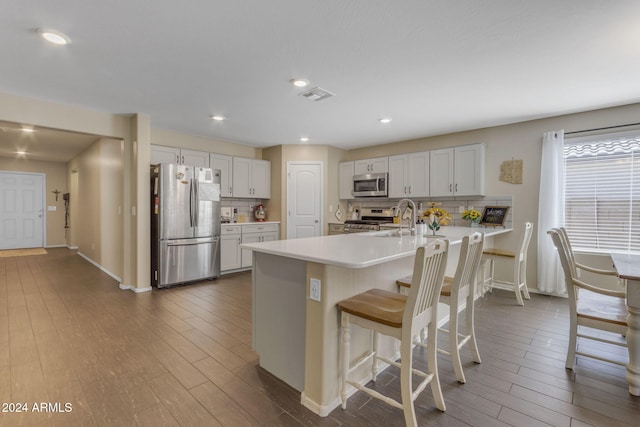 kitchen featuring a breakfast bar area, kitchen peninsula, stainless steel appliances, backsplash, and white cabinetry