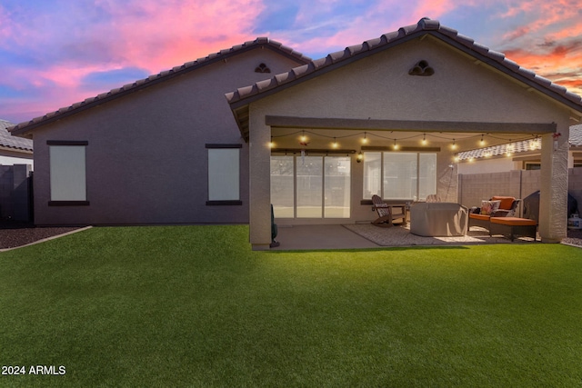 back house at dusk featuring a patio area and a lawn