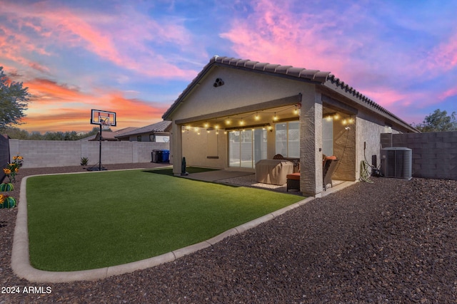 back house at dusk with a patio, cooling unit, and a lawn