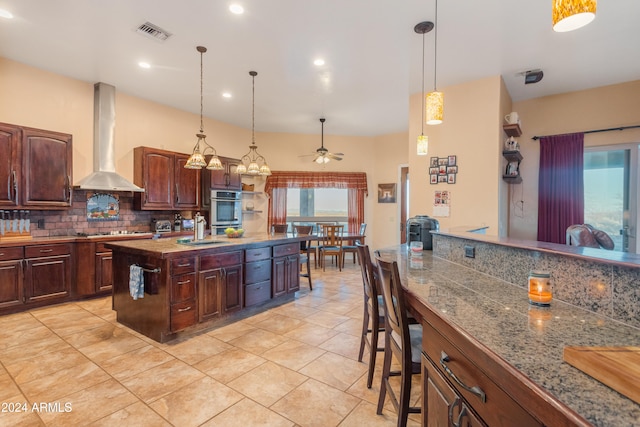 kitchen featuring tasteful backsplash, wall chimney exhaust hood, dark brown cabinetry, stainless steel appliances, and ceiling fan