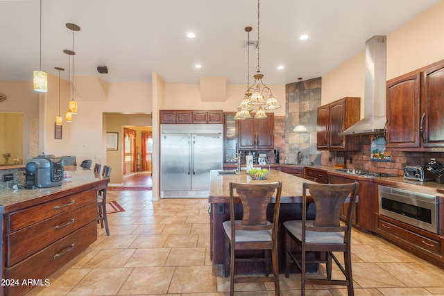 kitchen featuring appliances with stainless steel finishes, tasteful backsplash, wall chimney exhaust hood, decorative light fixtures, and a center island with sink