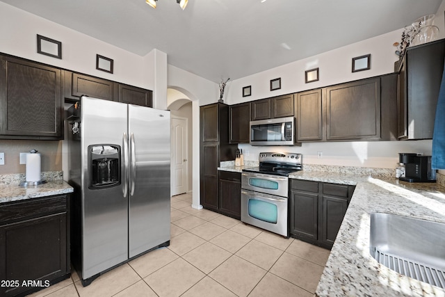 kitchen with dark brown cabinets, light stone countertops, light tile patterned floors, and appliances with stainless steel finishes