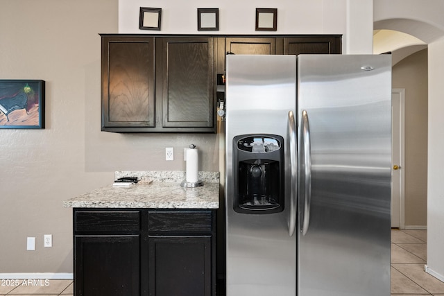 kitchen featuring stainless steel refrigerator with ice dispenser, light stone counters, light tile patterned floors, and dark brown cabinets