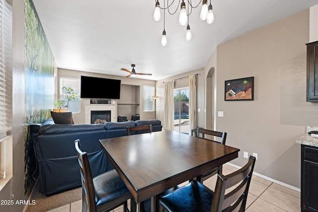 dining area featuring ceiling fan, plenty of natural light, a tiled fireplace, and light tile patterned flooring