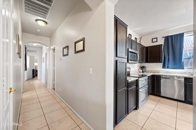 kitchen with light stone countertops, stainless steel appliances, dark brown cabinetry, and light tile patterned floors