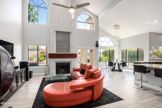 living room with beamed ceiling, light hardwood / wood-style flooring, a tiled fireplace, high vaulted ceiling, and ceiling fan