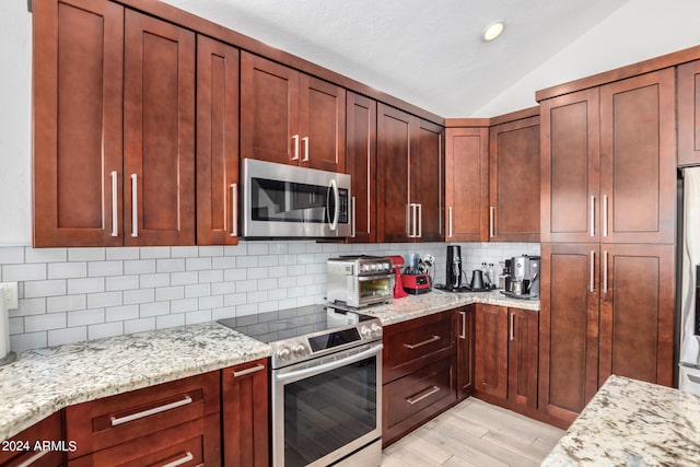 kitchen with stainless steel appliances, light stone counters, light hardwood / wood-style floors, decorative backsplash, and lofted ceiling