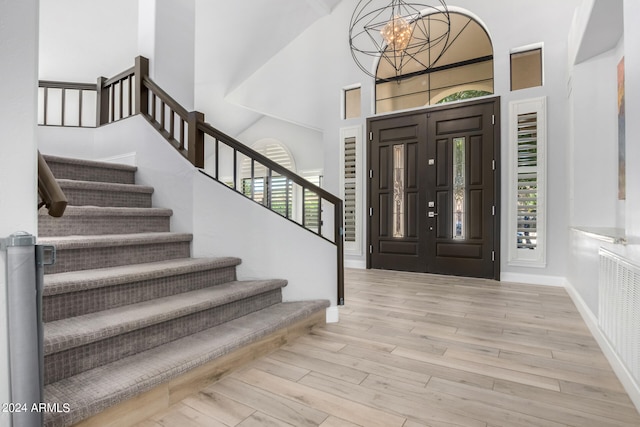 entryway featuring light hardwood / wood-style flooring, a towering ceiling, plenty of natural light, and a chandelier