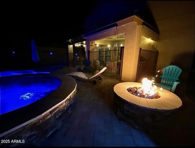 patio at twilight featuring fence, a fire pit, and a hot tub