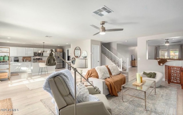 living room with visible vents, ceiling fan, stairs, and light wood finished floors