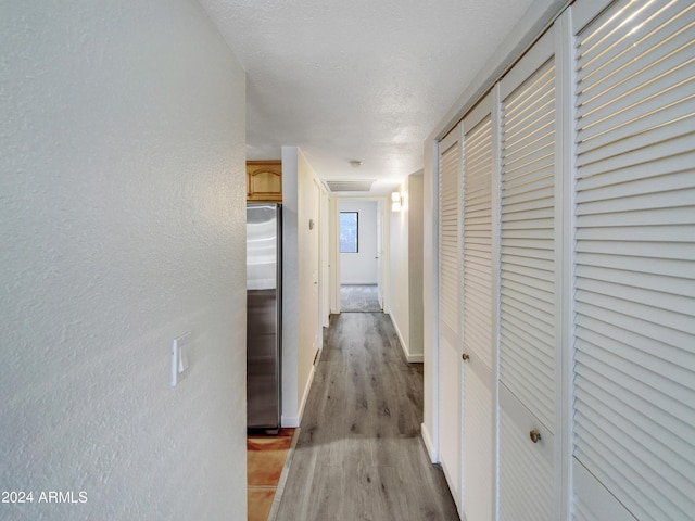 corridor with light wood-style floors, baseboards, a textured ceiling, and a textured wall