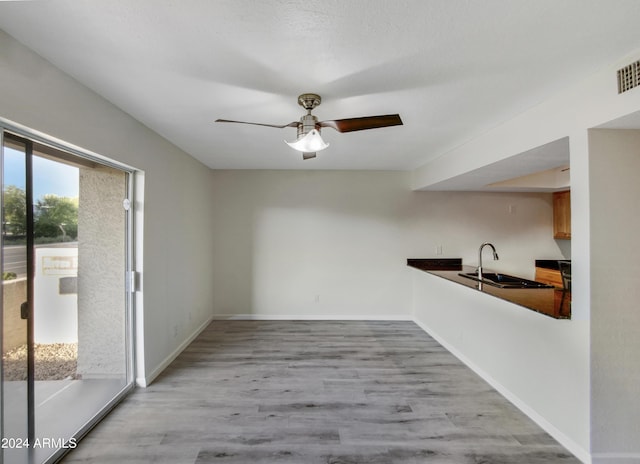 unfurnished dining area featuring a sink, ceiling fan, baseboards, and wood finished floors