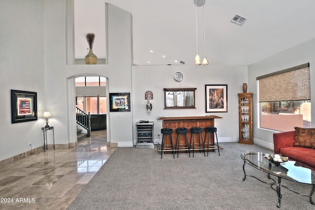 living area featuring visible vents, baseboards, a dry bar, stairs, and a towering ceiling