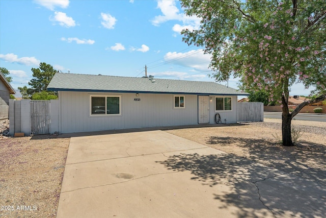 view of front of property featuring concrete driveway, fence, a patio area, and roof with shingles