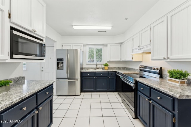 kitchen with appliances with stainless steel finishes, white cabinets, under cabinet range hood, a sink, and light tile patterned floors