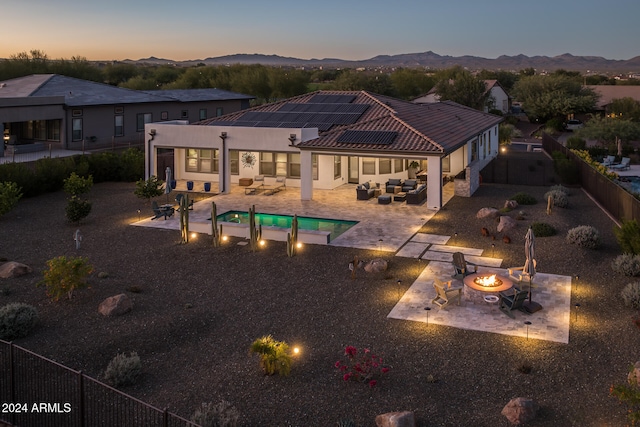 back house at dusk with solar panels, a mountain view, a fenced in pool, an outdoor living space with a fire pit, and a patio area