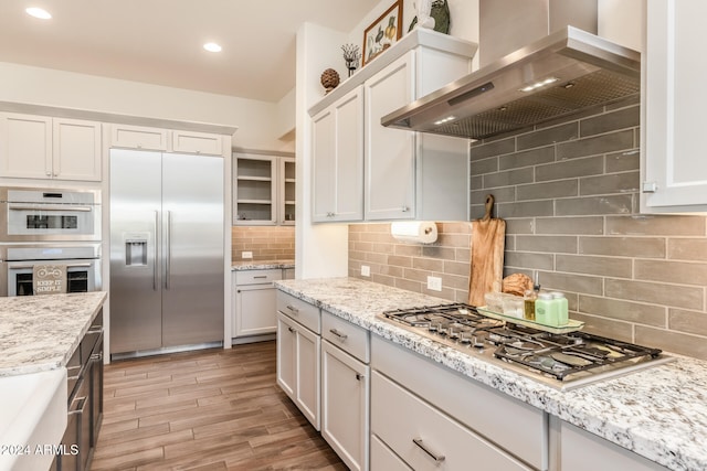 kitchen featuring backsplash, white cabinetry, wall chimney range hood, and appliances with stainless steel finishes