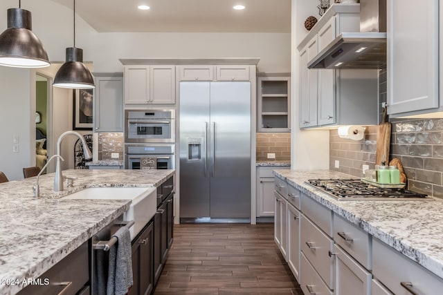 kitchen featuring dark wood-type flooring, hanging light fixtures, wall chimney exhaust hood, decorative backsplash, and appliances with stainless steel finishes