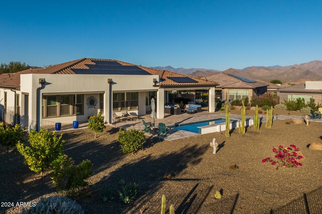 rear view of property featuring outdoor lounge area, solar panels, a mountain view, and a patio