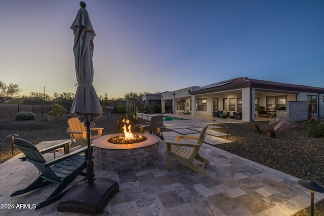 patio terrace at dusk with a fenced in pool and an outdoor fire pit