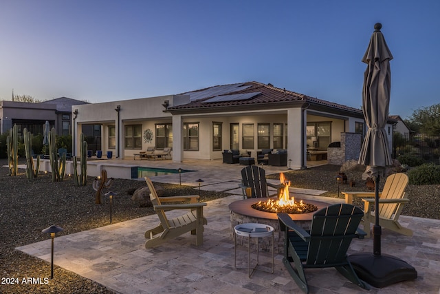 back house at dusk with solar panels, a patio, and an outdoor living space with a fire pit