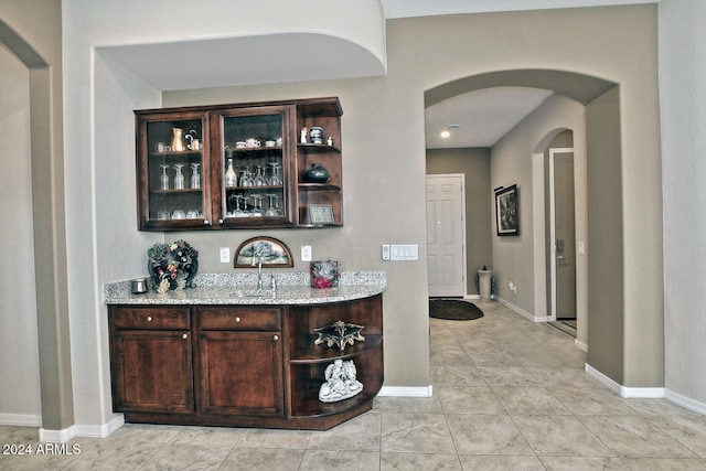 bar featuring light stone countertops and dark brown cabinets