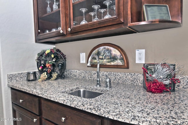 kitchen featuring light stone countertops, dark brown cabinets, and sink