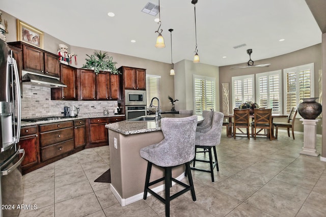 kitchen featuring pendant lighting, a kitchen island with sink, sink, light stone countertops, and stainless steel appliances