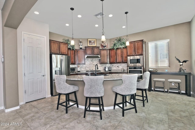 kitchen featuring sink, an island with sink, tasteful backsplash, decorative light fixtures, and stainless steel appliances