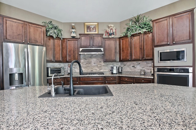 kitchen with dark brown cabinetry, light stone countertops, sink, decorative backsplash, and appliances with stainless steel finishes