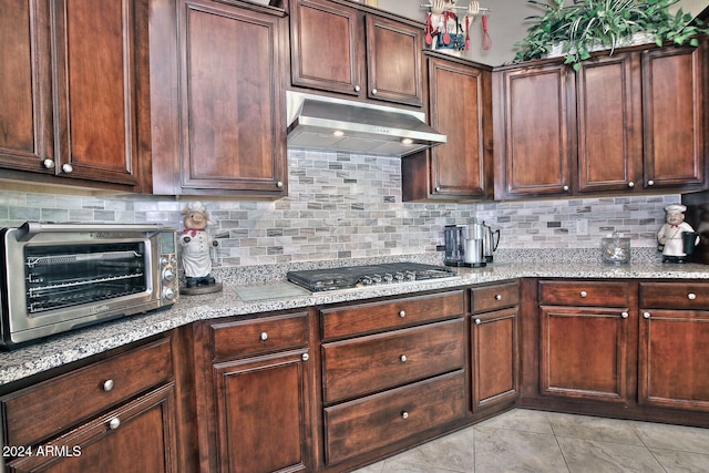 kitchen with backsplash, light tile patterned floors, dark brown cabinets, light stone counters, and stainless steel gas cooktop