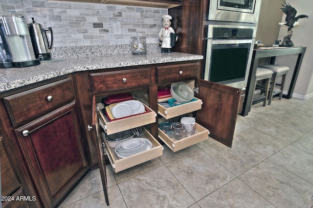 kitchen featuring decorative backsplash, stainless steel appliances, light stone countertops, and light tile patterned flooring