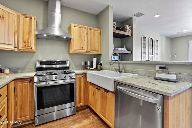 kitchen featuring appliances with stainless steel finishes, sink, wall chimney exhaust hood, light stone counters, and light hardwood / wood-style flooring