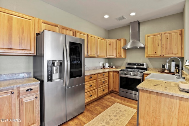 kitchen featuring sink, light wood-type flooring, stainless steel appliances, wall chimney exhaust hood, and light stone counters