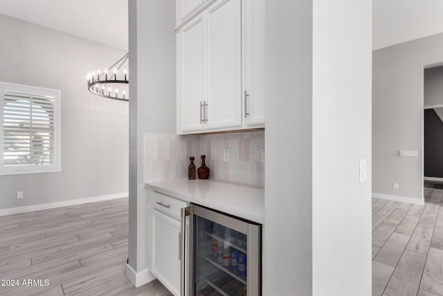 bar with white cabinets, light hardwood / wood-style flooring, beverage cooler, and backsplash