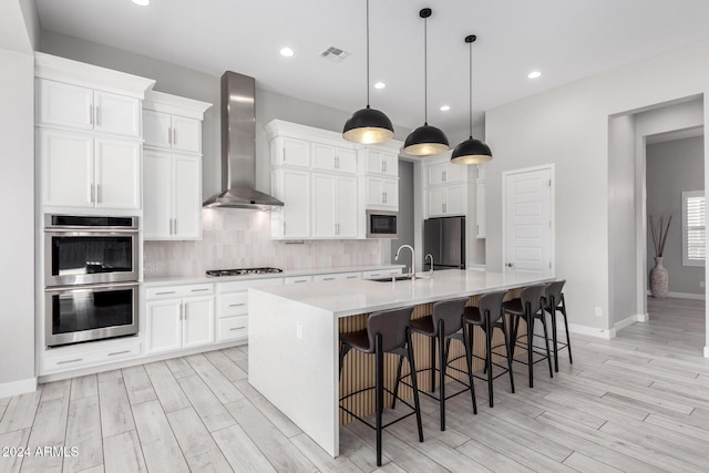 kitchen featuring a center island with sink, black microwave, double oven, wall chimney exhaust hood, and fridge