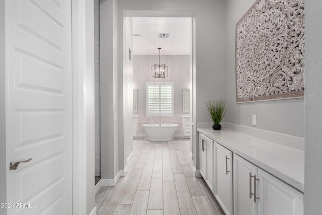 bathroom featuring wood-type flooring, vanity, a tub to relax in, and a notable chandelier