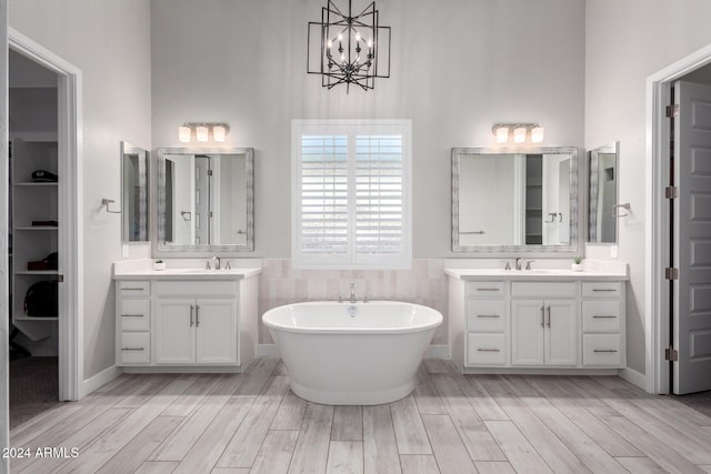 bathroom with tile walls, vanity, an inviting chandelier, and a bath