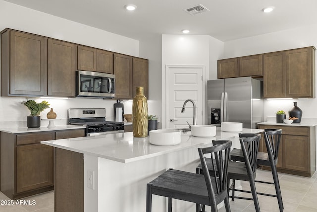 kitchen featuring a breakfast bar area, a center island with sink, light tile patterned floors, and appliances with stainless steel finishes